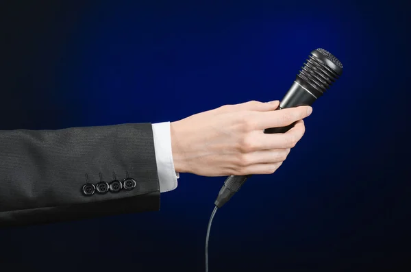 Ділова мова і тема: чоловік у чорному костюмі тримає чорний мікрофон на темно-синьому фоні в студії ізольовані — стокове фото