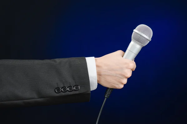 Тема бізнесу та мови: Чоловік у чорному костюмі тримає мікрофон на сірому темно-синьому ізольованому фоні в студії — стокове фото