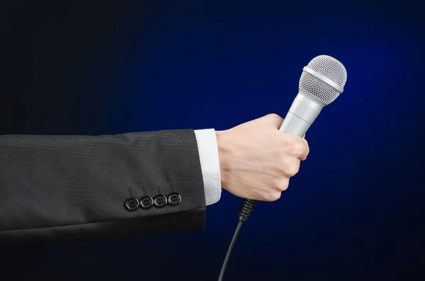 Business and speech topic: Man in black suit holding a microphone on a gray dark blue isolated background in studio — Stockfoto