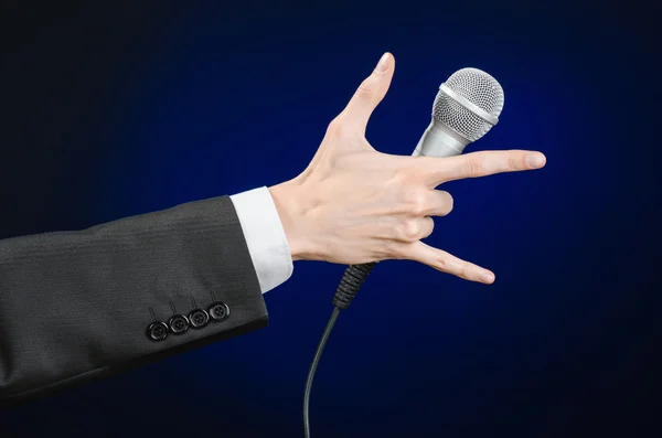 Тема бізнесу та мови: Чоловік у чорному костюмі тримає мікрофон на сірому темно-синьому ізольованому фоні в студії — стокове фото