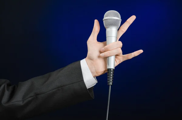 Business and speech topic: Man in black suit holding a microphone on a gray dark blue isolated background in studio — Stockfoto