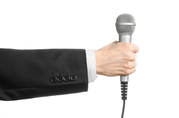Тема бізнесу та мови: Чоловік у чорному костюмі тримає сірий мікрофон на ізольованому білому тлі в студії — стокове фото