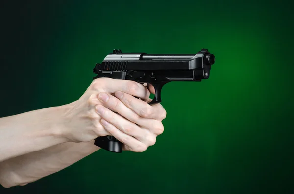 Firearms and murderer topic: human hand holding a gun on a dark green background isolated in studio — Stock Photo, Image