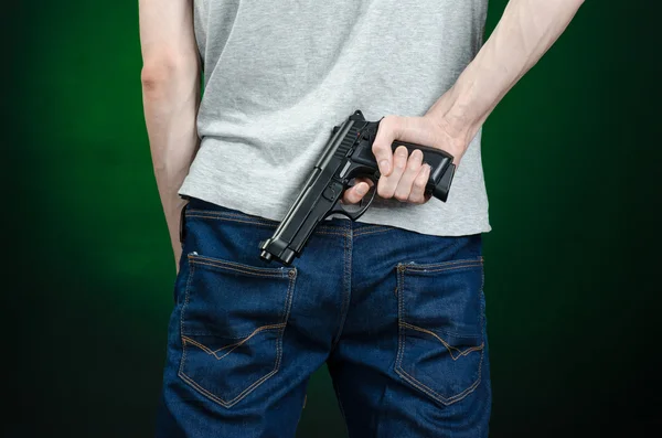 Armas de fuego y tema asesino: hombre con una camiseta gris sosteniendo un arma sobre un fondo verde oscuro aislado en el estudio — Foto de Stock