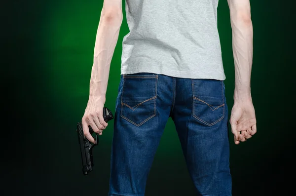 Firearms and murderer topic: man in a gray t-shirt holding a gun on a dark green background isolated in studio — Stock Photo, Image