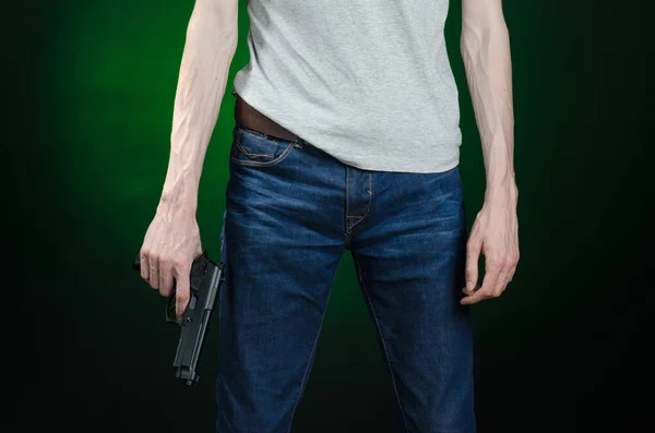 Armas de fuego y tema asesino: hombre con una camiseta gris sosteniendo un arma sobre un fondo verde oscuro aislado en el estudio —  Fotos de Stock