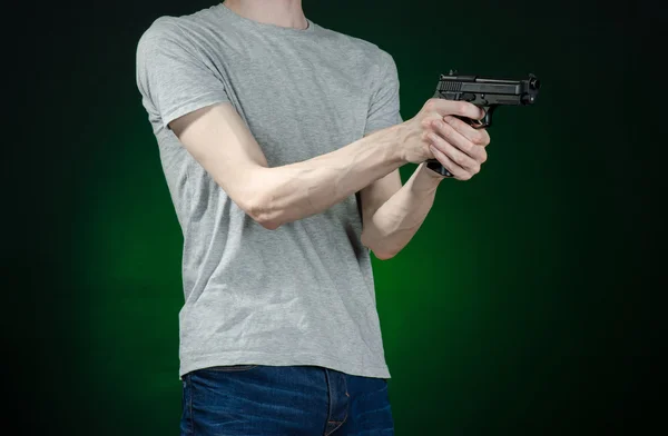 Armas de fuego y tema asesino: hombre con una camiseta gris sosteniendo un arma sobre un fondo verde oscuro aislado en el estudio — Foto de Stock