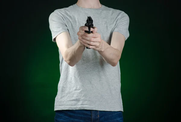 Firearms and murderer topic: man in a gray t-shirt holding a gun on a dark green background isolated in studio — 스톡 사진