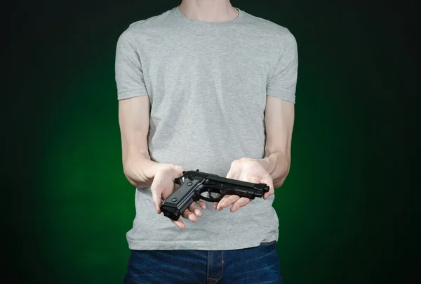 Armas de fuego y tema asesino: hombre con una camiseta gris sosteniendo un arma sobre un fondo verde oscuro aislado en el estudio — Foto de Stock