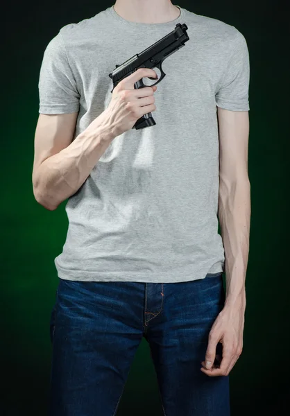 Tópico de armas de fogo e assassino: homem com uma camiseta cinza segurando uma arma em um fundo verde escuro isolado em estúdio — Fotografia de Stock