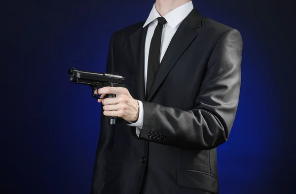 Firearms and security topic: a man in a black suit holding a gun on a dark blue background in studio isolated — 图库照片