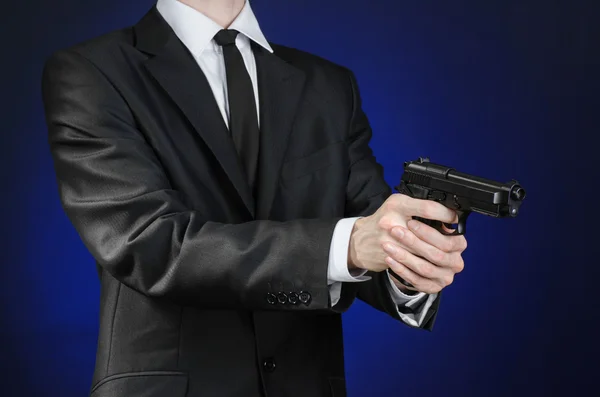 Firearms and security topic: a man in a black suit holding a gun on a dark blue background in studio isolated — Φωτογραφία Αρχείου
