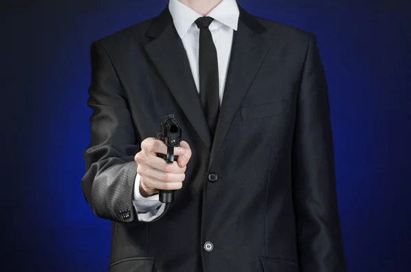 Firearms and security topic: a man in a black suit holding a gun on a dark blue background in studio isolated — Stock Fotó