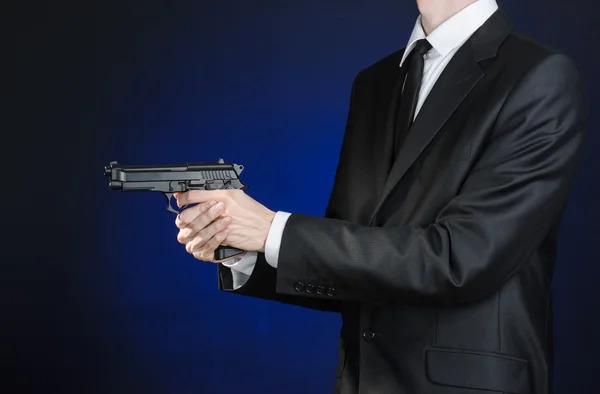 Schusswaffen und Sicherheitsthema: ein Mann im schwarzen Anzug mit Waffe auf dunkelblauem Hintergrund im Studio isoliert — Stockfoto