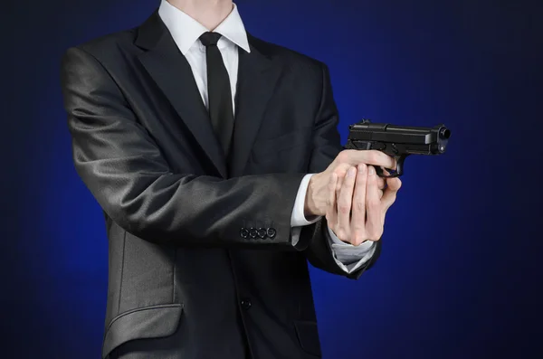 Schusswaffen und Sicherheitsthema: ein Mann im schwarzen Anzug mit Waffe auf dunkelblauem Hintergrund im Studio isoliert — Stockfoto