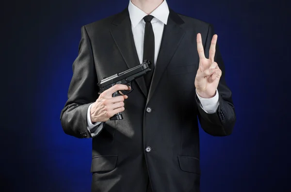 Firearms and security topic: a man in a black suit holding a gun on a dark blue background in studio isolated — 图库照片