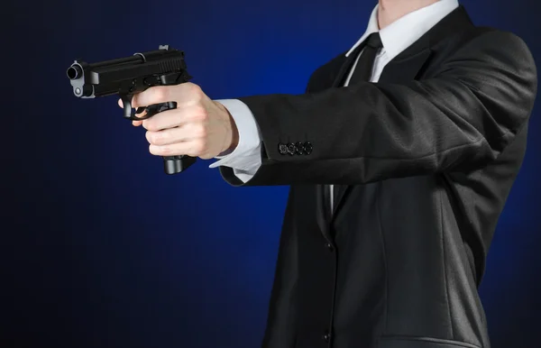 Огнестрельное оружие и тема безопасности: человек в черном костюме, держащий пистолет на темно-синем фоне в изолированной студии — стоковое фото