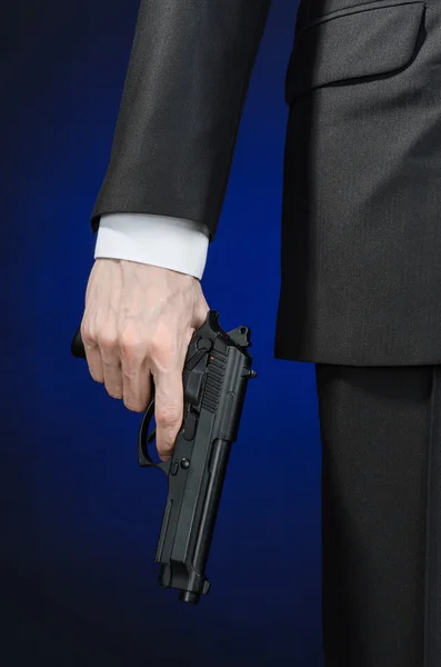 Firearms and security topic: a man in a black suit holding a gun on a dark blue background in studio isolated — Stok fotoğraf