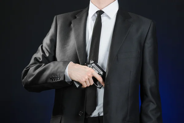 Firearms and security topic: a man in a black suit holding a gun on a dark blue background in studio isolated — 스톡 사진