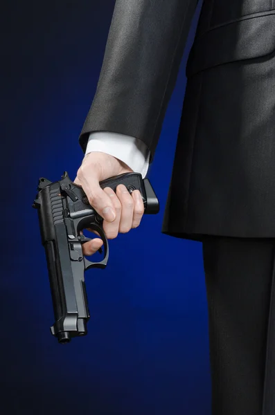 Firearms and security topic: a man in a black suit holding a gun on a dark blue background in studio isolated — Stok fotoğraf