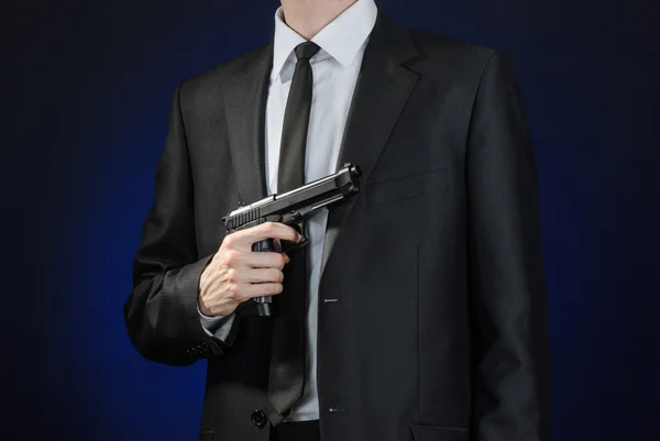 Зброя та тема безпеки: чоловік у чорному костюмі тримає пістолет на темно-синьому тлі в студії ізольований — стокове фото
