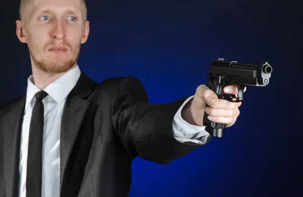 Firearms and security topic: a man in a black suit holding a gun on a dark blue background in studio isolated — 图库照片