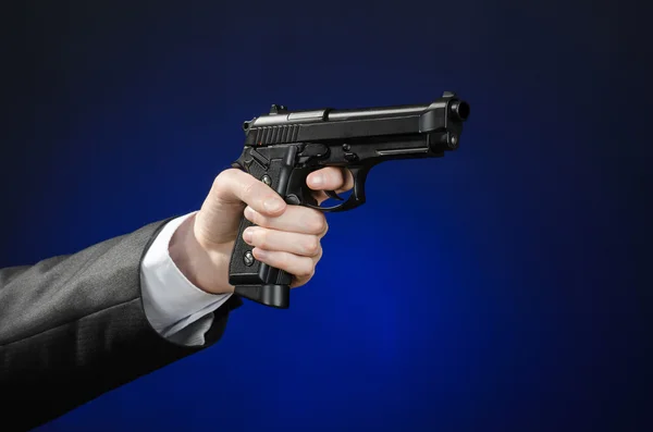 Firearms and security topic: a man in a black suit holding a gun on a dark blue background in studio isolated — Stok fotoğraf