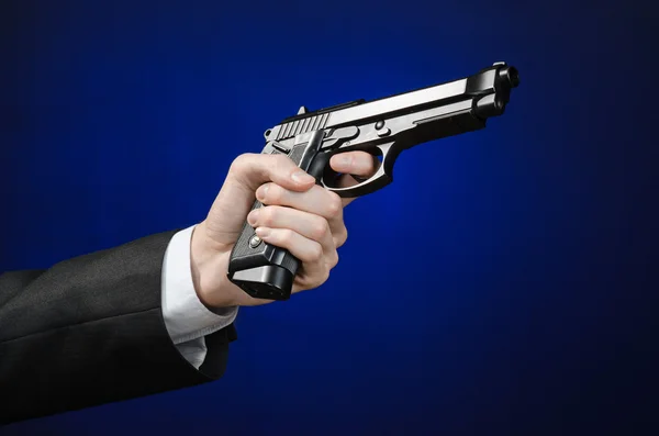Firearms and security topic: a man in a black suit holding a gun on a dark blue background in studio isolated — Stok fotoğraf