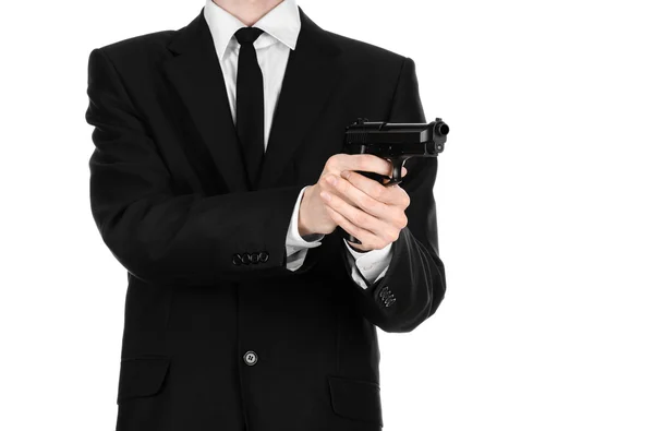 Armas de fuego y temas de seguridad: un hombre con un traje negro sosteniendo un arma sobre un fondo blanco aislado en el estudio —  Fotos de Stock