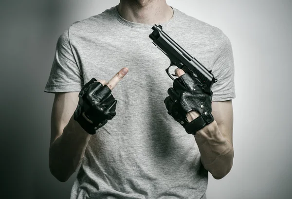 Тема жахів і вогнепальної зброї: вбивця з пістолетом в руці в чорних рукавичках на сірому фоні в студії — стокове фото