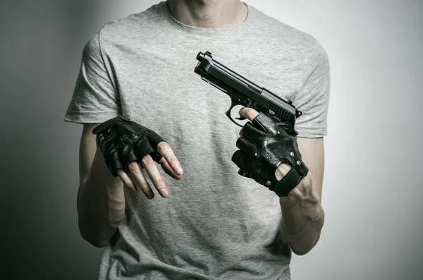 Tema de terror y armas de fuego: el asesino con una pistola en la mano con guantes negros sobre un fondo gris en el estudio — Foto de Stock