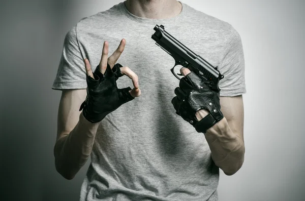Tópico de terror e armas de fogo: o assassino com uma arma na mão em luvas pretas em um fundo cinza no estúdio — Fotografia de Stock