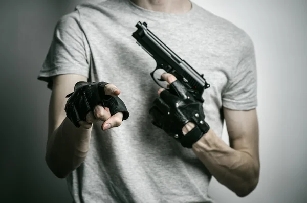 Horror and firearms topic: the killer with a gun in his hand in black gloves on a gray background in the studio — 스톡 사진
