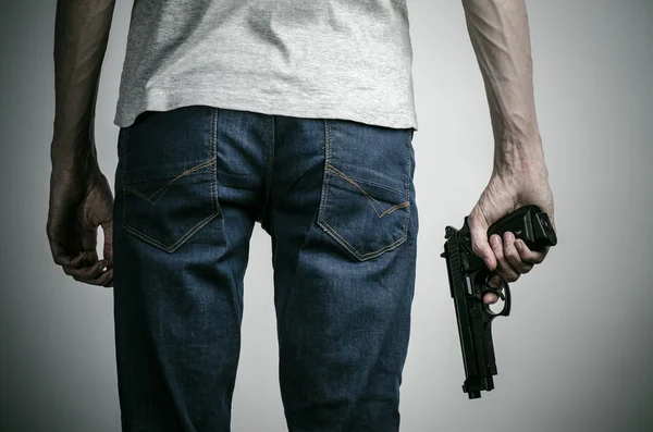 Tema de terror y armas de fuego: asesino enloquecido con un arma sobre un fondo gris en el estudio — Foto de Stock