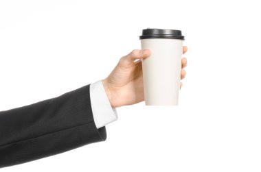 Business lunches coffee theme: businessman in a black suit holding a white blank paper cup of coffee with a brown plastic cap isolated on a white background in the studio, advertising coffee