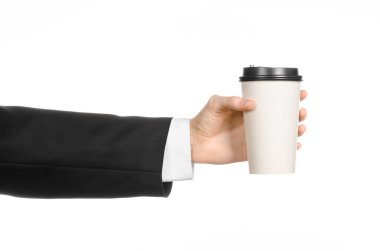 Business lunches coffee theme: businessman in a black suit holding a white blank paper cup of coffee with a brown plastic cap isolated on a white background in the studio, advertising coffee