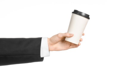 Business lunches coffee theme: businessman in a black suit holding a white blank paper cup of coffee with a brown plastic cap isolated on a white background in the studio, advertising coffee