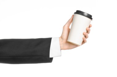 Business lunches coffee theme: businessman in a black suit holding a white blank paper cup of coffee with a brown plastic cap isolated on a white background in the studio, advertising coffee