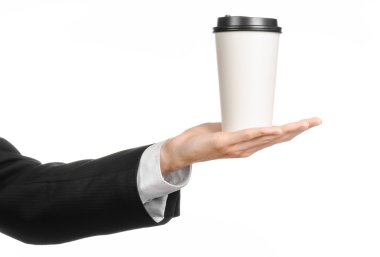 Business lunches coffee theme: businessman in a black suit holding a white blank paper cup of coffee with a brown plastic cap isolated on a white background in the studio, advertising coffee