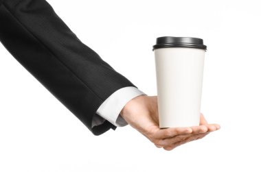 Business lunches coffee theme: businessman in a black suit holding a white blank paper cup of coffee with a brown plastic cap isolated on a white background in the studio, advertising coffee