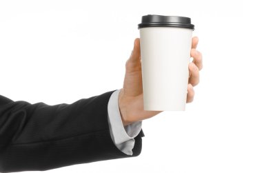 Business lunches coffee theme: businessman in a black suit holding a white blank paper cup of coffee with a brown plastic cap isolated on a white background in the studio, advertising coffee