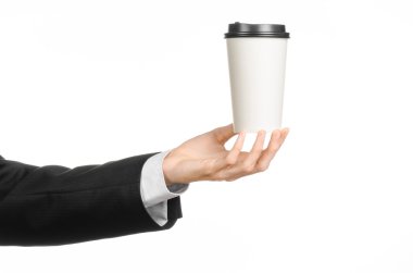 Business lunches coffee theme: businessman in a black suit holding a white blank paper cup of coffee with a brown plastic cap isolated on a white background in the studio, advertising coffee