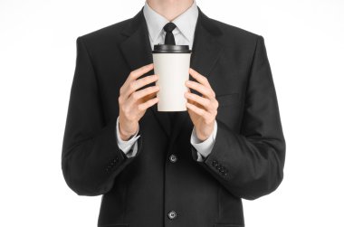 Business lunches coffee theme: businessman in a black suit holding a white blank paper cup of coffee with a brown plastic cap isolated on a white background in the studio, advertising coffee