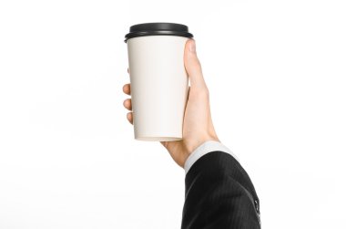 Business lunches coffee theme: businessman in a black suit holding a white blank paper cup of coffee with a brown plastic cap isolated on a white background in the studio, advertising coffee