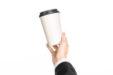 Business lunches coffee theme: businessman in a black suit holding a white blank paper cup of coffee with a brown plastic cap isolated on a white background in the studio, advertising coffee