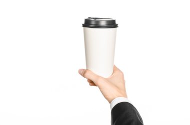 Business lunches coffee theme: businessman in a black suit holding a white blank paper cup of coffee with a brown plastic cap isolated on a white background in the studio, advertising coffee