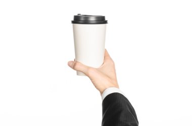 Business lunches coffee theme: businessman in a black suit holding a white blank paper cup of coffee with a brown plastic cap isolated on a white background in the studio, advertising coffee