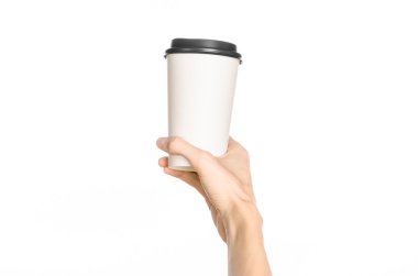 Breakfast and coffee theme: man's hand holding white empty paper coffee cup with a brown plastic cap isolated on a white background in the studio, advertising of coffee first-person view