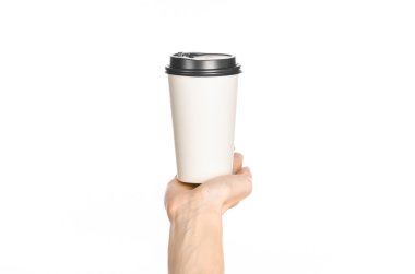 Breakfast and coffee theme: man's hand holding white empty paper coffee cup with a brown plastic cap isolated on a white background in the studio, advertising of coffee first-person view