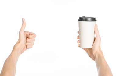 Breakfast and coffee theme: man's hand holding white empty paper coffee cup with a brown plastic cap isolated on a white background in the studio, advertising of coffee first-person view